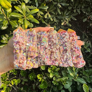 May include: Six iridescent rainbow aura quartz crystal points in various shades of pink, orange, and yellow. The points are clustered together and have a rough, natural texture.
