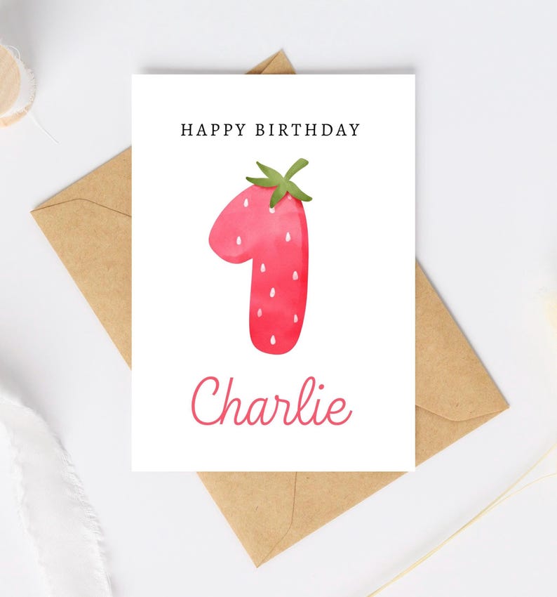May include: A white card with the text "Happy Birthday" and a red watercolor strawberry shaped like the number one. The name "Charlie" is written in cursive below the number.