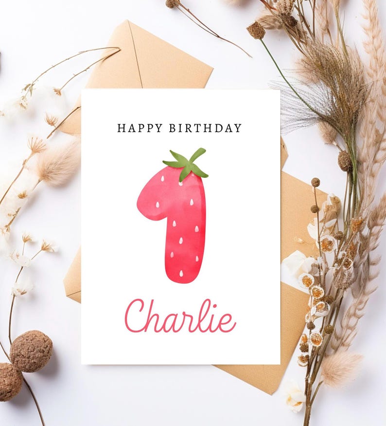 May include: A white card with the text "Happy Birthday" and a red strawberry shaped like the number one. The name "Charlie" is written below the number one.