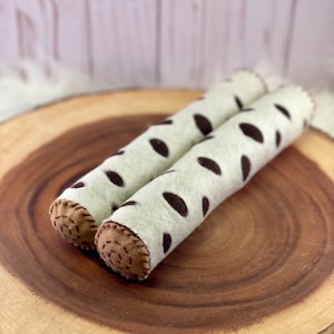 May include: Two brown and white felt logs with brown stitching. The logs are on a wooden surface.