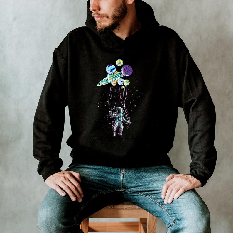 Peut inclure: Sweat &agrave; capuche noir avec un motif color&eacute; d'un astronaute tenant des plan&egrave;tes et un anneau de type Saturne, sur fond &eacute;toil&eacute;. Le motif est imprim&eacute; sur le devant du sweat &agrave; capuche.