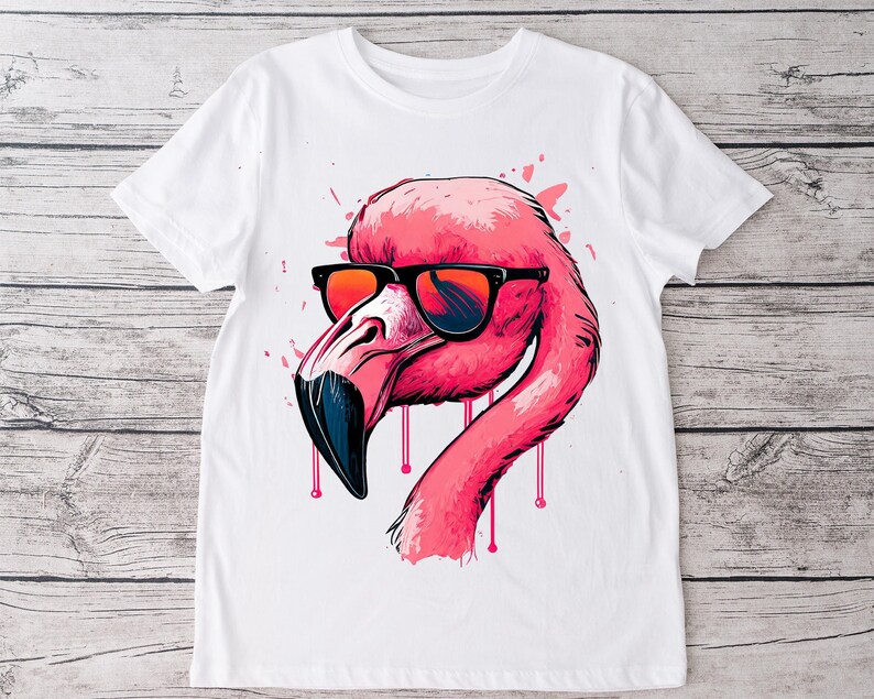 May include: White t-shirt featuring a pink flamingo wearing sunglasses. The flamingo has a black beak and is set against a background of pink paint splatters. The flamingo's neck has pink drips.