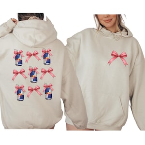 a woman wearing a white hoodie with pink bows and a graphic of a can of Red Bull on the back.