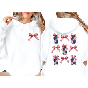A white hoodie with a graphic design on the back featuring multiple red bows and cans of Red Bull energy drink.