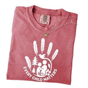 A red t-shirt with a white handprint design and the text "EVERY CHILD MATTERS" printed on it.