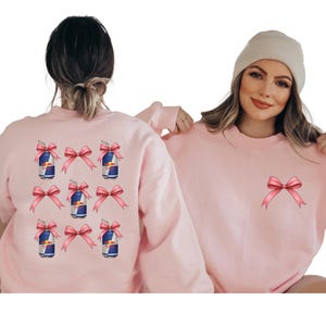 two women wearing pink sweaters with pink bows on the back.