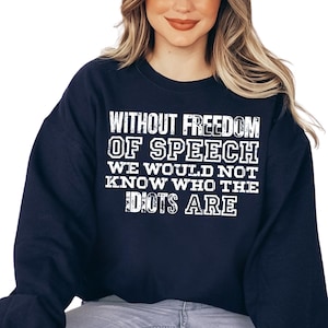 May include: A navy blue crewneck sweatshirt featuring white distressed-style lettering that reads: WITHOUT FREEDOM OF SPEECH WE WOULD NOT KNOW WHO THE IDIOTS ARE. The garment has long sleeves and a ribbed neckline, providing a standard fit and casual look.
