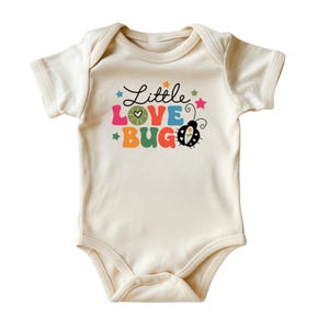 May include: A cream-colored baby onesie with a colorful graphic that says "Little Love Bug" with a ladybug illustration.