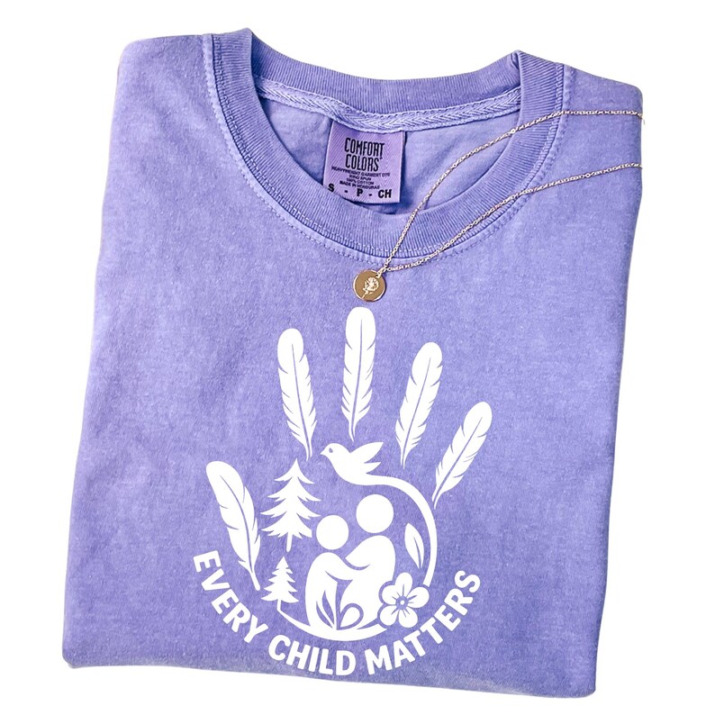 A purple t-shirt with a white handprint design and the text "EVERY CHILD MATTERS" printed on it.