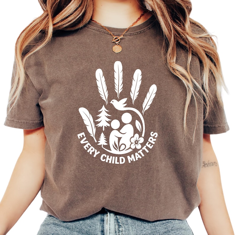 A woman wearing a brown t-shirt with a white graphic design that says "Every Child Matters".