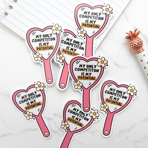 May include: Six pink heart-shaped hand mirror stickers with the text "My only competition is my potential" in black lettering and a gold rectangle with the word "potential" inside. The stickers have white flowers and glitter accents.