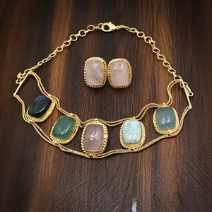 May include: A gold-toned necklace and earring set featuring rectangular cabochon gemstones in shades of black, green, pink, and light blue. The necklace has a multi-strand chain design with five bezel-set stones, while the earrings match.