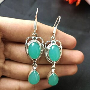 May include: A pair of silver-toned drop earrings featuring oval and teardrop-shaped, light teal-colored gemstones. The earrings have a decorative design around the oval stones and a hook closure.