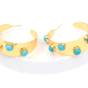 May include: A pair of gold-tone hoop earrings. Each earring features three round, turquoise-colored stones set along the front. The earrings have a hammered texture and a post closure.