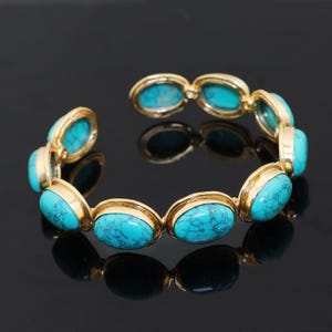 May include: Gold-plated bracelet with oval turquoise stones. The bracelet has a hinged design, with each turquoise stone set in a gold bezel. The stones are a vibrant blue-green colour with dark veining.