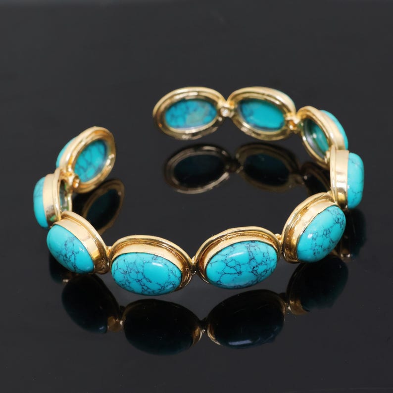 May include: Gold-plated bracelet with oval turquoise stones. The bracelet has a hinged design, with each turquoise stone set in a gold bezel. The stones are a vibrant blue-green colour with dark veining.
