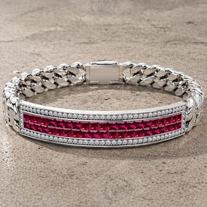 Pode incluir: Pulseira de prata com um centro retangular com duas fileiras de pedras vermelhas quadradas. O centro é delimitado por pequenas pedras transparentes. A pulseira tem um design de elos de corrente.