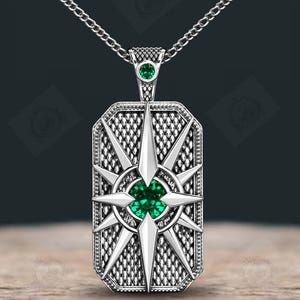 Puede incluir: Collar con colgante de plata con un colgante rectangular con un diseño de brújula. El colgante tiene una piedra preciosa verde central y está suspendido de una cadena de plata. El diseño de la brújula tiene múltiples puntas y un fondo texturizado.