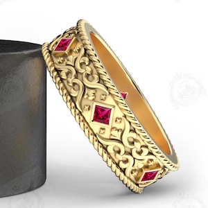 Puede incluir: Un anillo de banda de oro con un diseño adornado detallado y cuatro piedras cuadradas rojas.