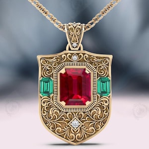 Puede incluir: Collar con colgante dorado con un colgante en forma de escudo con intrincados adornos. El colgante presenta una gran gema roja rectangular en el centro, flanqueada por dos gemas verdes. Pequeños diamantes añaden brillo. La cadena del collar también es dorada.