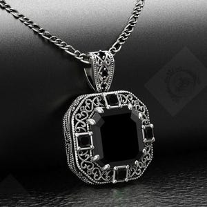 May include: A silver-toned pendant necklace with a large, square black gemstone at the center. The pendant is intricately detailed with filigree and smaller black stones. The chain is a simple, linked design.