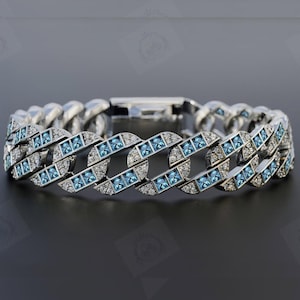 May include: A silver-toned bracelet with a curb chain design. The bracelet features alternating sections of light blue square-cut stones and clear, small stones. The clasp is also silver-toned.