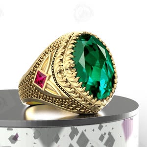 May include: A gold ring featuring a large, oval-shaped green gemstone and a smaller, square-shaped red gemstone. The ring has an intricate, ornate design.