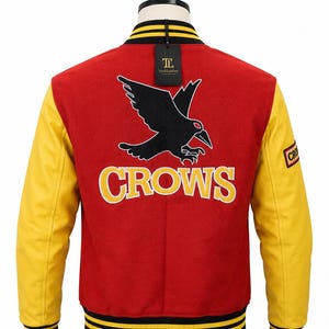 May include: A red and yellow varsity jacket featuring a black crow graphic and the word CROWS in yellow lettering on the back. The jacket has yellow sleeves, a black and yellow striped collar and cuffs, and a black tag attached to the neckline.