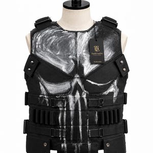 May include: A black tactical vest featuring a large, distressed white skull graphic on the front. The vest includes adjustable side straps, multiple utility loops, and metal snap buttons at the hem. A black TandiLeather brand tag is attached to the chest.