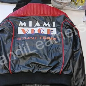 May include: Black leather jacket with red accents and the text "MIAMI VICE STUNT TEAM" on the back. The jacket has a quilted red panel on the upper back and red trim. A classic style.