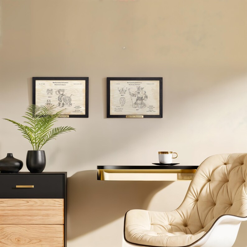 Puede incluir: Dos impresiones de patentes enmarcadas con marcos negros y placas doradas cuelgan de una pared beige. Un aparador negro y de madera con un jarr&oacute;n negro y una planta en maceta est&aacute;n en primer plano. Una taza de t&eacute; blanca y dorada se encuentra en un estante negro.