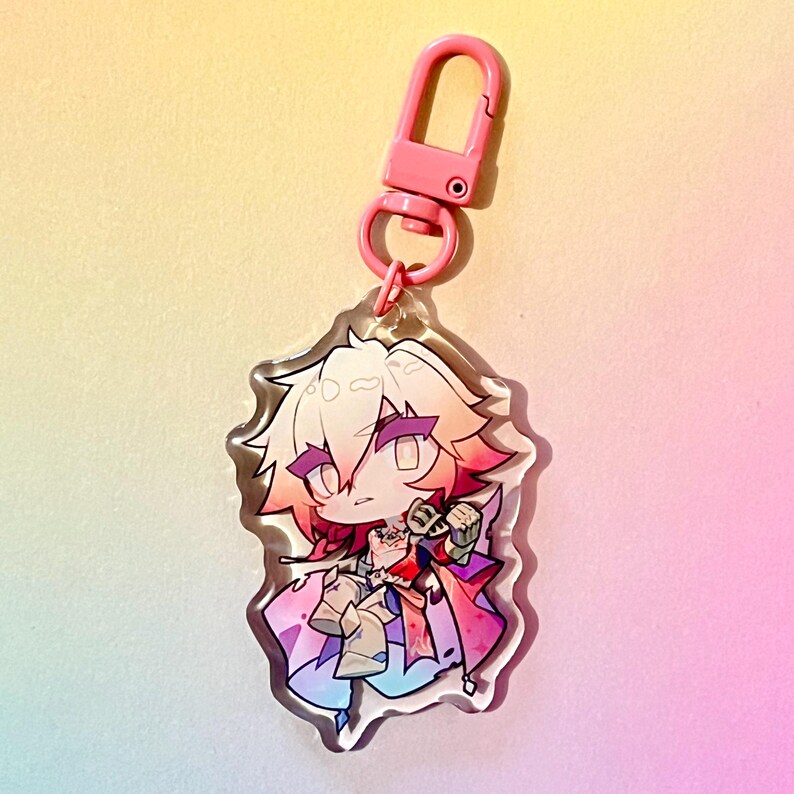 Puede incluir: Un llavero de un personaje de anime rosa y blanco con un cierre de metal rosa. El personaje tiene el pelo largo, rosa y blanco, y lleva un atuendo colorido.