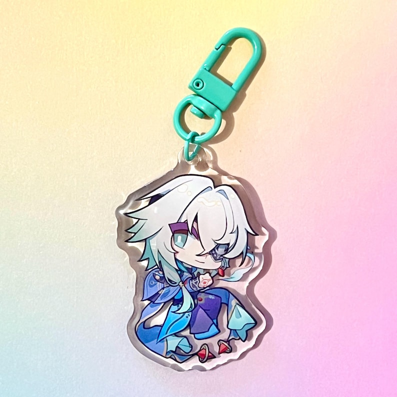 Puede incluir: Un llavero de acr&iacute;lico transparente con un personaje de anime chibi de pelo blanco, ojos azules y un atuendo azul y morado. El llavero tiene un cierre met&aacute;lico verde.