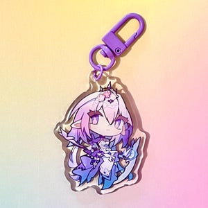 Puede incluir: Un llavero de un personaje de anime morado y azul con un clip morado. El personaje tiene el pelo largo rosa, un vestido blanco y una cola de drag&oacute;n azul y blanca.
