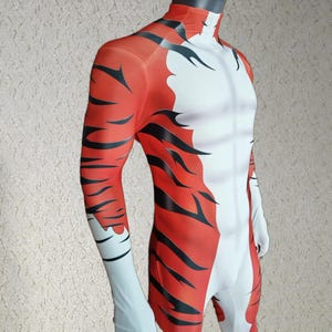 Op de afbeelding: Een volledig gestreept tijgerkostuum in rood, zwart en wit. Het kostuum heeft een coltrui en lange mouwen. Het ontwerp bootst het patroon van een tijger na, met zwarte strepen op een rode achtergrond en witte accenten.