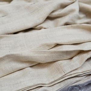 May include: A close-up of a stack of off-white fabric. The fabric has a woven texture and is folded neatly.