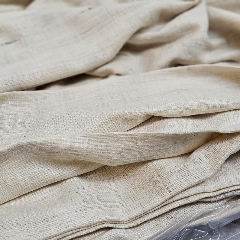 May include: A close-up of a stack of off-white fabric. The fabric has a woven texture and is folded neatly.