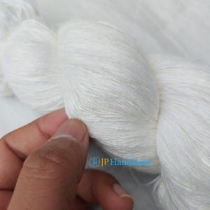 Puede incluir: Una madeja de hilo de seda blanco, con una textura suave y delicada. El hilo está enrollado de forma suelta y parece estar hilado a mano.