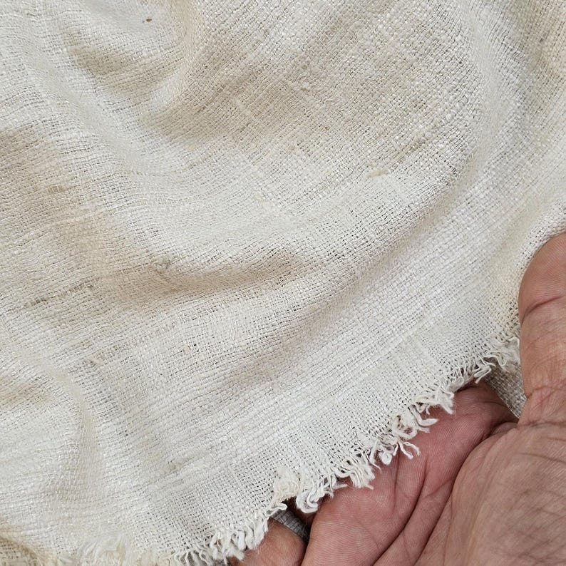 May include: Close-up of a white, woven fabric with a frayed edge. The fabric has a slightly textured surface and is made of natural fibers.