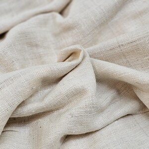 May include: Close-up of a natural off-white fabric with a textured weave. The fabric is folded and draped, showing its soft and drapey texture.
