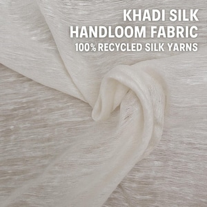 May include: Close-up of Khadi silk handloom fabric made from 100% recycled silk yarns. The fabric is a light cream color, with a slightly textured appearance. The text "KHADI SILK HANDLOOM FABRIC 100% RECYCLED SILK YARNS" is visible in white.