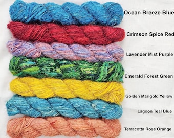 May include: A collection of colorful yarn skeins in shades of blue, red, purple, green, yellow, teal, and orange. Each skein is labeled with its color name, including "Ocean Breeze Blue" and "Terracotta Rose Orange". Ideal for knitting and crochet projects.