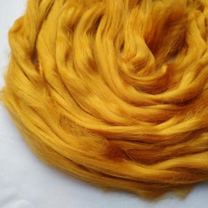 May include: A close-up of a pile of golden yellow wool roving. The wool is soft and fluffy, and it is perfect for spinning or felting.