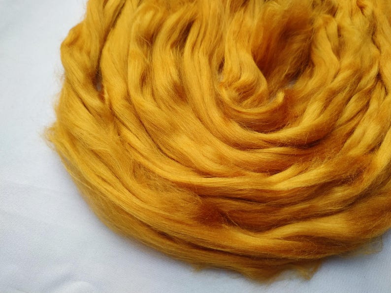 May include: A close-up of a pile of golden yellow wool roving. The wool is soft and fluffy, and it is perfect for spinning or felting.