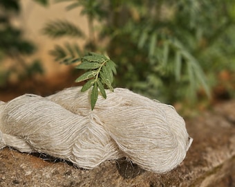 May include: A close-up of a skein of off-white yarn, possibly silk, with a natural, textured appearance. The yarn is labeled "JPHANDLOOM Finest Quality Recycled Sari Silk Feswa Yarn". A small green leaf rests on top of the yarn.
