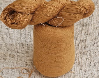 Peut inclure: Gros plan sur deux écheveaux de fil de couleur brun doré. L'un est enroulé en forme de cône, l'autre est enroulé en spirale sur le dessus. Le fil a un aspect doux et texturé, suggérant des fibres naturelles. Le fond est un tissu texturé blanc cassé.