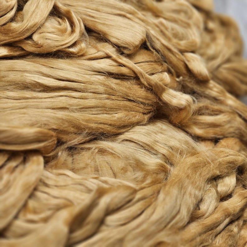 May include: Close-up of a pile of light brown, natural fibers. The fibers are soft and fluffy, and they are arranged in a random pattern.