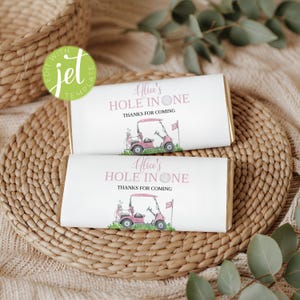 Pode incluir: Duas embalagens retangulares de barra de chocolate com fundo branco e texto rosa que diz Alice's HOLE IN ONE e THANKS FOR COMING. O design inclui uma ilustração em aquarela de um carrinho de golfe rosa, uma bolsa de golfe e uma bandeira.