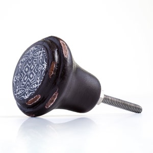 May include: A dark brown cabinet knob with a black and white geometric design. The knob has a metal screw for attaching to a cabinet door.