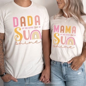 May include: Two white t-shirts with a rainbow design and the text "Dada of the little ray of sunshine" and "Mama of the little ray of sunshine".